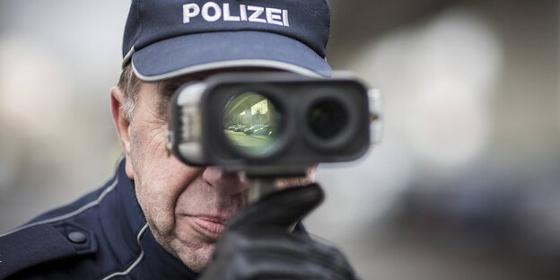 Mann mit Polizeimütze schaut durch eine Art Fernglas Mann mit Polizeimütze schaut durch eine Art Fernglas