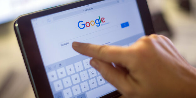 Eine Hand tippt auf ein Tablet etwas in die Suchmaschine Google ein Eine Hand tippt auf ein Tablet etwas in die Suchmaschine Google ein