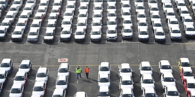 Vogelperspektive auf einen Parkplatz, auf dem ganz viele Autos stehen - zwei Menschen laufen dazwischen umher Vogelperspektive auf einen Parkplatz, auf dem ganz viele Autos stehen - zwei Menschen laufen dazwischen umher