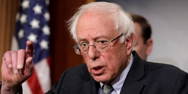 Präsidentschaftskandidat Bernie Sanders mit erhobener Hand vor US-Flagge Präsidentschaftskandidat Bernie Sanders mit erhobener Hand vor US-Flagge
