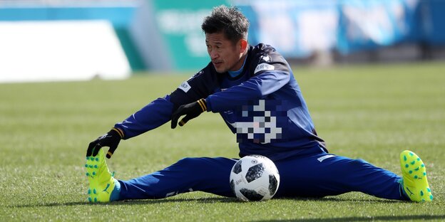 Der japanische Fußballer Miura sitzt auf dem Fußballfeld und vor ihm liegt ein Fußball Der japanische Fußballer Miura sitzt auf dem Fußballfeld und vor ihm liegt ein Fußball