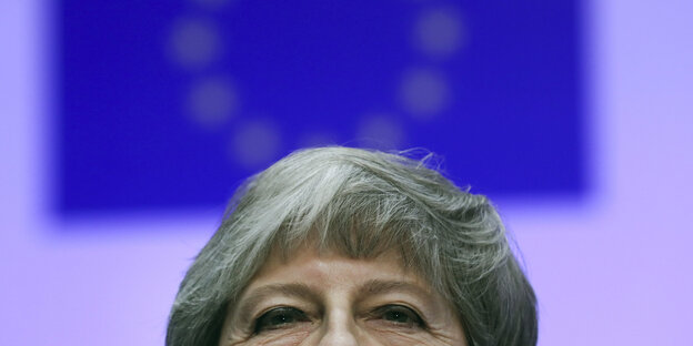 Nahaufnahme von der oberen Hälfte von Theresa Mays Gesicht vor einer EU-Flagge Nahaufnahme von der oberen Hälfte von Theresa Mays Gesicht vor einer EU-Flagge