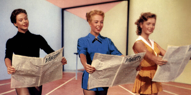Bild von 1953: Drei Frauen stehen in einem Raum und haben eine Zeitung in der Hand Bild von 1953: Drei Frauen stehen in einem Raum und haben eine Zeitung in der Hand