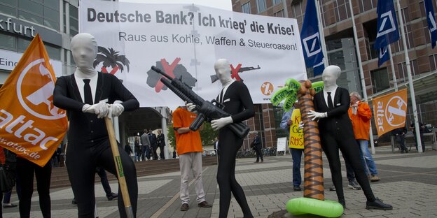 Menschen in Anzügen und mit weißen Masken protestieren mit Schildern vor der Deutschen Bank in Frankfurt. Menschen in Anzügen und mit weißen Masken protestieren mit Schildern vor der Deutschen Bank in Frankfurt.