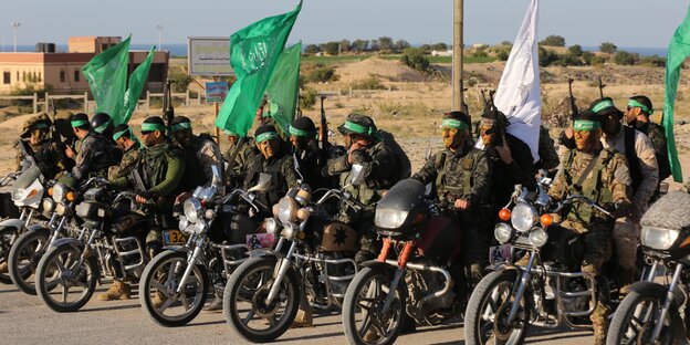 Männer auf Motorrädern halten grüne Flaggen hoch.