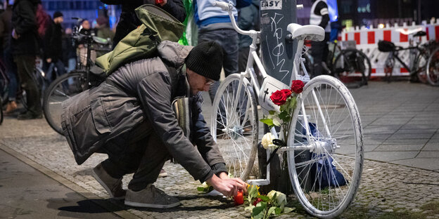 Ein Mann legt Blumen an ein weißes Fahrrad Ein Mann legt Blumen an ein weißes Fahrrad