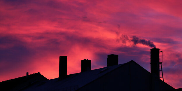 Aus einem Kamin steigt Rauch in einen roten Abendhimmel Aus einem Kamin steigt Rauch in einen roten Abendhimmel
