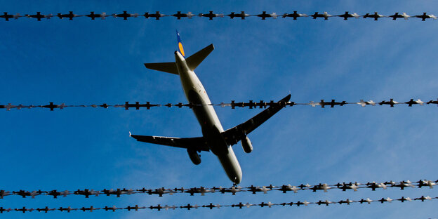 EIn Flugzeug am Himmel hinter Stacheldraht.