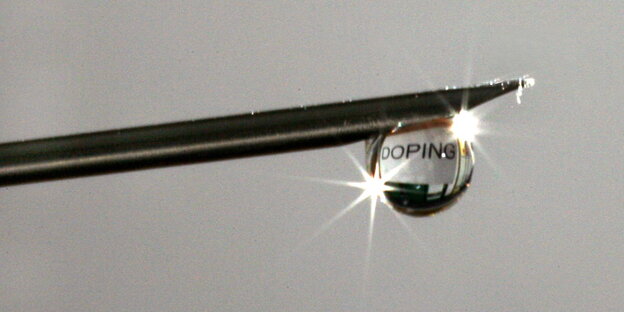 an der Spitze einer Kanüle hängt ein Tropfen auf dem sich das Wort „Doping“ spiegelt an der Spitze einer Kanüle hängt ein Tropfen auf dem sich das Wort „Doping“ spiegelt
