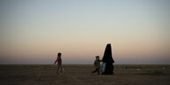 Eine Frau in Niqap läuft mit zwei Kindern durch die Landschaft.
