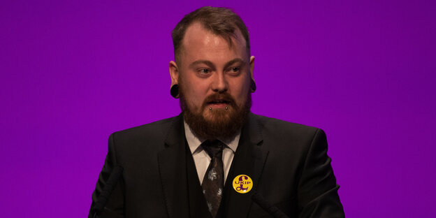 Mark Meechan trägt einen Ukip-Button und steht vor einer lilafarbenen Wand Mark Meechan trägt einen Ukip-Button und steht vor einer lilafarbenen Wand