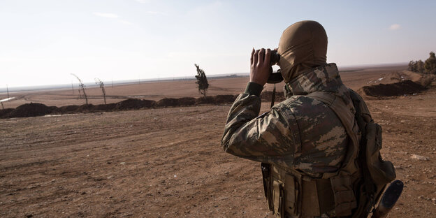 YPG-Soldat steht auf einer freien Fläche in Syrien und blickt durch ein Fernglas YPG-Soldat steht auf einer freien Fläche in Syrien und blickt durch ein Fernglas