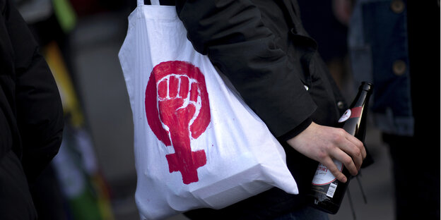 ein stoffbeutel mit einem feministischen symbol, eine geballte faust in dem symbol für frau, hängt einer person über die schulter ein stoffbeutel mit einem feministischen symbol, eine geballte faust in dem symbol für frau, hängt einer person über die schulter