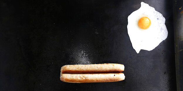 Perspektive von oben auf einen Grill: Darauf brutzeln zwei Würste und ein Spiegelei Perspektive von oben auf einen Grill: Darauf brutzeln zwei Würste und ein Spiegelei