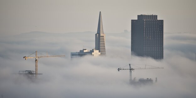 Hochhäuser und zwei Kräne ragen aus den Wolken über einer Stadt hervor Hochhäuser und zwei Kräne ragen aus den Wolken über einer Stadt hervor