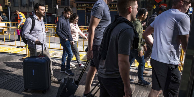 Menschen mit Rollkoffern gehen auf einem Fußgängerweg auf der Rambla in Barcelona Menschen mit Rollkoffern gehen auf einem Fußgängerweg auf der Rambla in Barcelona