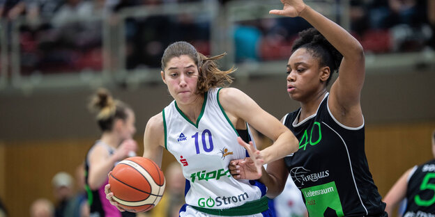 Zwei Frauen, die auf einem Spielfeld in einer Halle um einen Basketball kämpfen Zwei Frauen, die auf einem Spielfeld in einer Halle um einen Basketball kämpfen