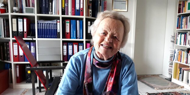 Eine Frau sitzt vor einem Bücherregal und schaut in die Kamera Eine Frau sitzt vor einem Bücherregal und schaut in die Kamera