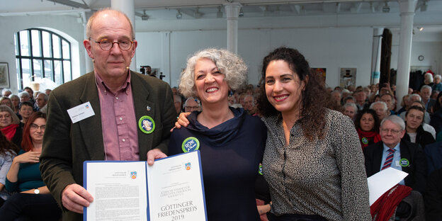 Preisträgerin Iris Hefets zwischen Laudatorin Nirit Sommerfeld (r.) und Juror Andreas Zumach. Letzterer hält die Auszeichnungsurkunde in die Höhe Preisträgerin Iris Hefets zwischen Laudatorin Nirit Sommerfeld (r.) und Juror Andreas Zumach. Letzterer hält die Auszeichnungsurkunde in die Höhe