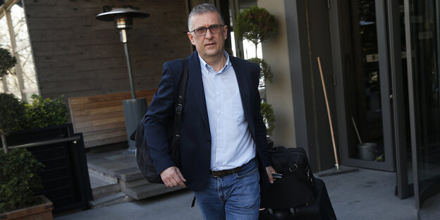 Mann im Sakko verlässt eilig Hotel mit Rollkoffer Mann im Sakko verlässt eilig Hotel mit Rollkoffer