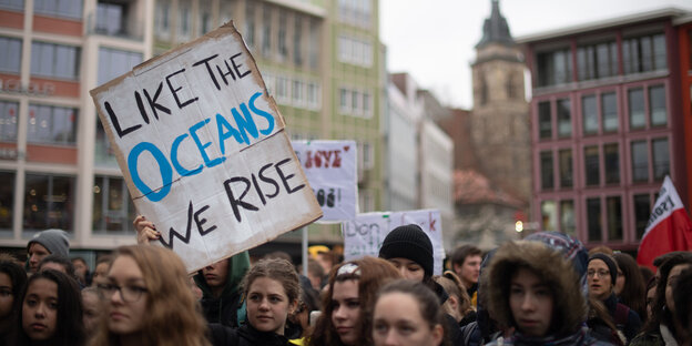 Eine Teilnehmerin hält während der Klimaschutz-Demonstration «Fridays for Future» ein Schild hoch, auf dem «Like the oceans we rise» steht Eine Teilnehmerin hält während der Klimaschutz-Demonstration «Fridays for Future» ein Schild hoch, auf dem «Like the oceans we rise» steht
