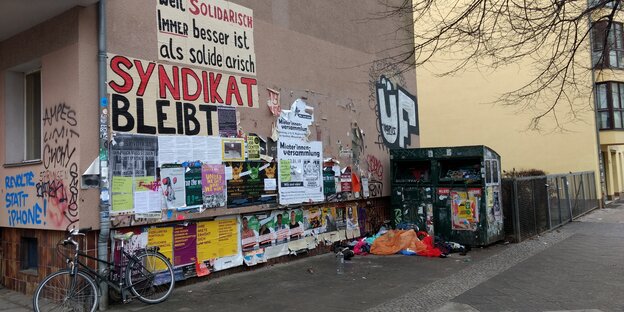 Eine Hauswand im Schillerkiez, die mittels Plakatierung das Bleiben des Syndikats fordert Eine Hauswand im Schillerkiez, die mittels Plakatierung das Bleiben des Syndikats fordert