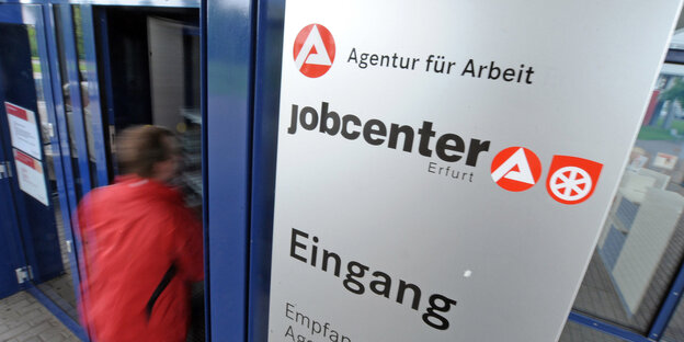 Ein Mann geht durch eine Tür. Am Eingangschild steht Jobcenter