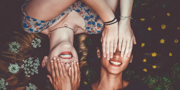 Zwei lachende Frauen halten sich gegenseitig die Augen zu Zwei lachende Frauen halten sich gegenseitig die Augen zu