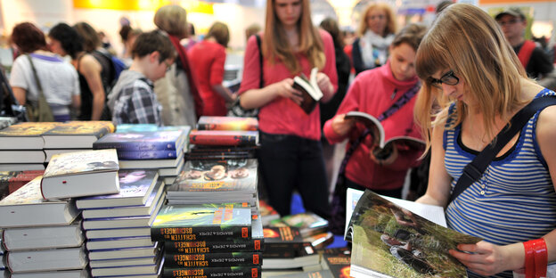 Jugendliche Mädchen stehen auf der Buchmesse vor Bücherstapeln und lesen jeweils in einem Buch Jugendliche Mädchen stehen auf der Buchmesse vor Bücherstapeln und lesen jeweils in einem Buch
