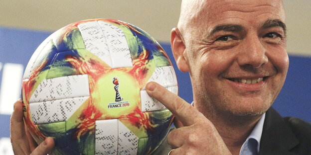 Gianni Infantino grinst und hält einen Fußball in der Hand