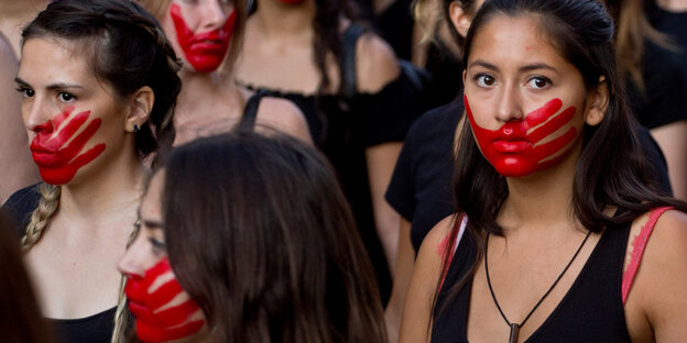 Mehrere Frauen bei einer Demonstration, sie haben rote Farbe im Gesicht, die die Form einer Hand hat Mehrere Frauen bei einer Demonstration, sie haben rote Farbe im Gesicht, die die Form einer Hand hat