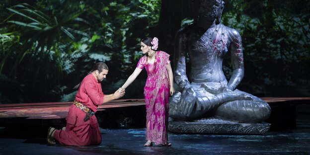 Vor einer Buddhastatue kniet ein Mann von einer Frau, beide in Saris Vor einer Buddhastatue kniet ein Mann von einer Frau, beide in Saris