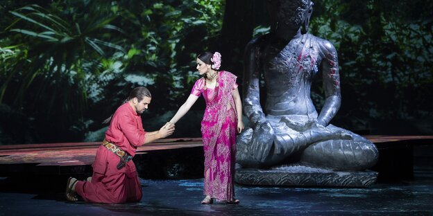 Vor einer Buddhastatue kniet ein Mann von einer Frau, beide in Saris