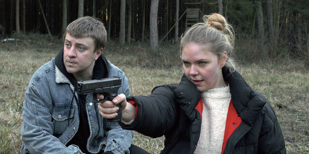 Ein junger Mann und eine junge Frau, sie zielt mit einer Waffe auf etwas Ein junger Mann und eine junge Frau, sie zielt mit einer Waffe auf etwas