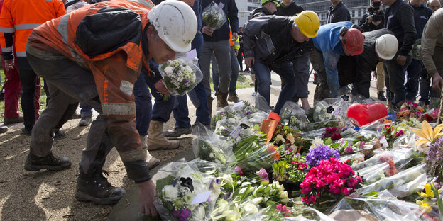Menschen mit Signalwesten und Schutzhelmen legen Blumen auf den Boden. Menschen mit Signalwesten und Schutzhelmen legen Blumen auf den Boden.