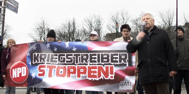 Udoi Voigt steht mit einem Mikrofon in der Hand vor einem NPD-Transparent mit der Aufschrift "Kriegstreiber stoppen - Ami go home" Udoi Voigt steht mit einem Mikrofon in der Hand vor einem NPD-Transparent mit der Aufschrift "Kriegstreiber stoppen - Ami go home"