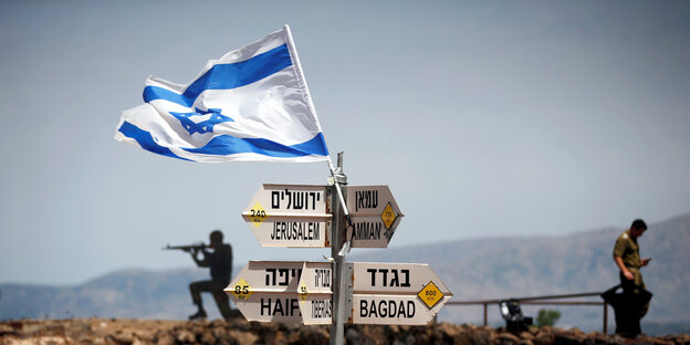 Ein Wegweiser mit Pfeilen in verschiedene Richtungen, darüber weht die israelische Flagge. Im Hintergrund sind Soldaten zu sehen Ein Wegweiser mit Pfeilen in verschiedene Richtungen, darüber weht die israelische Flagge. Im Hintergrund sind Soldaten zu sehen