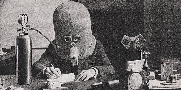 Ein Mensch mit einer Maske sitzt an einem Schreibtisch. Ein Mensch mit einer Maske sitzt an einem Schreibtisch.