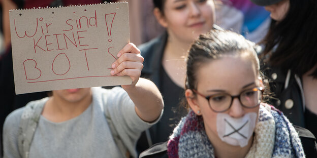 Eine Frau mit zugeklebtem Mund und eine, die en Plakat hochhält, laufen auf einer Demonstration Eine Frau mit zugeklebtem Mund und eine, die en Plakat hochhält, laufen auf einer Demonstration