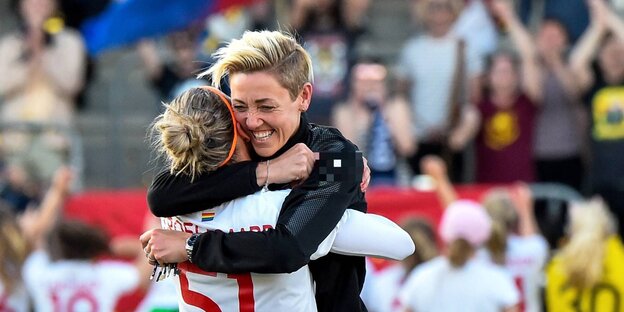 zwei Frauen umarmen sich, im Hintergrund eine volle Tribüne zwei Frauen umarmen sich, im Hintergrund eine volle Tribüne