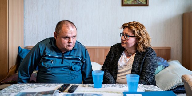 Ein Mann und eine Frau sitzen nachdenklich an einem Tisch in einer aufgeräumten Wohnung Ein Mann und eine Frau sitzen nachdenklich an einem Tisch in einer aufgeräumten Wohnung