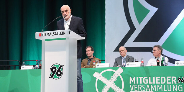 Martin Kind steht hinter einem Rednerpult mit 96-Logo. Martin Kind steht hinter einem Rednerpult mit 96-Logo.