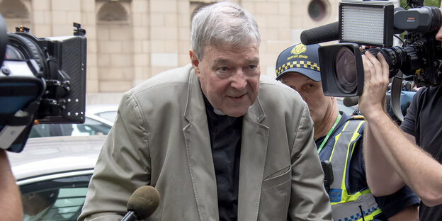 George Pell steht zwischen Fernsehkameras und Mikrofonen