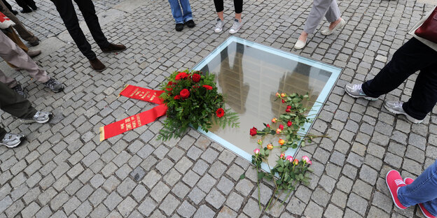 Blumenkränze liegen auf einer eingelassenen Scheibe auf einem gepflasterten Platz Blumenkränze liegen auf einer eingelassenen Scheibe auf einem gepflasterten Platz