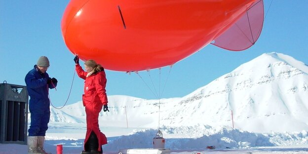 Eine Forscherin und ein Forscher in Schneeanzügen starten einen Wetterballon. Eine Forscherin und ein Forscher in Schneeanzügen starten einen Wetterballon.