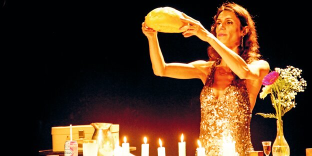 Eine Frau in einem goldglänzenden Kleid hält ein Brot über einem Tisch mit Kerzen hoch. Eine Frau in einem goldglänzenden Kleid hält ein Brot über einem Tisch mit Kerzen hoch.