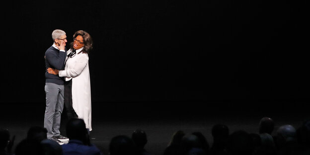 Apple-Chef Tim Cook und Moderatorin Oprah Winfrey umarmen sich vor einem schwarzen Hintergrund Apple-Chef Tim Cook und Moderatorin Oprah Winfrey umarmen sich vor einem schwarzen Hintergrund