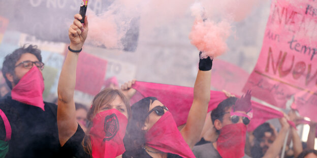 Frauen mit pinkem Mundschutz zünden pinke Bengalos. Frauen mit pinkem Mundschutz zünden pinke Bengalos.