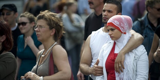 Zuschauer unter freiem Himmel: darunter eine ältere weiße Dame in kurzem Tshirt und ein jüngeres Pärchen, sie mit Kopftuch Zuschauer unter freiem Himmel: darunter eine ältere weiße Dame in kurzem Tshirt und ein jüngeres Pärchen, sie mit Kopftuch