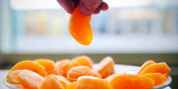 Mandarinenstücke auf einem Teller, Hand nimmt eine weg Mandarinenstücke auf einem Teller, Hand nimmt eine weg